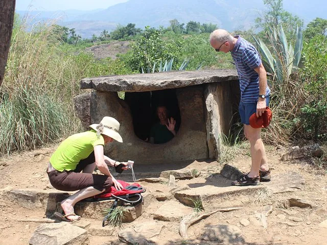 Turistas explorando una antigua estructura de dolmen de piedra en un paisaje de matorral.