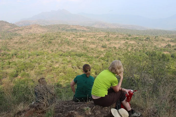 Tourists sitting on a rock, admiring a vast hilly landscape.
